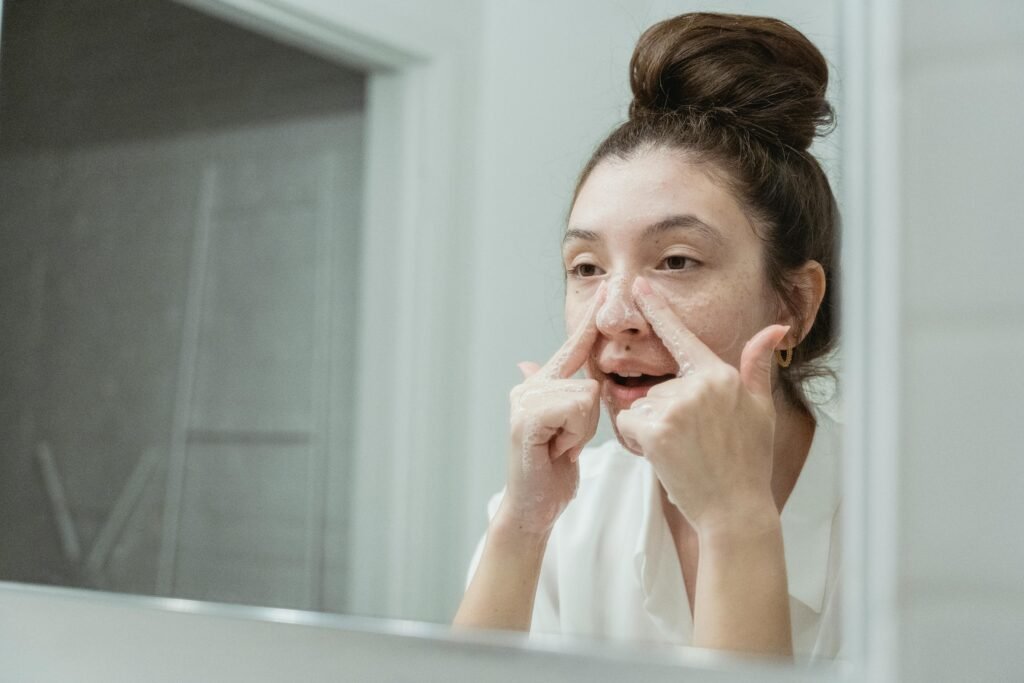 A young woman applies skincare in front of a bathroom mirror, focusing on facial care.